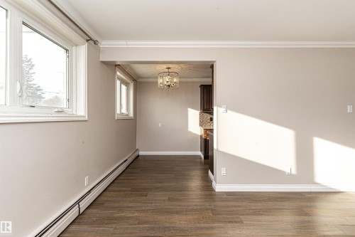 Spare room with baseboard heating, a chandelier, dark wood-style flooring, and crown molding - 102 10735 81 Avenue, Edmonton, AB - Indoor Photo Showing Other Room