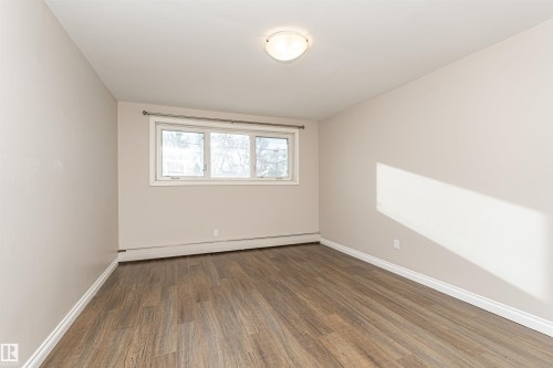 Unfurnished room featuring wood finished floors and a baseboard radiator - 102 10735 81 Avenue, Edmonton, AB - Indoor Photo Showing Other Room