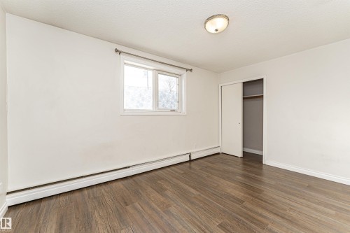 Unfurnished bedroom featuring a baseboard heating unit, dark wood-style flooring, a closet, and a textured ceiling - 102 10735 81 Avenue, Edmonton, AB - Indoor Photo Showing Other Room