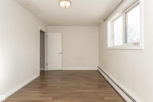 Unfurnished room with a baseboard heating unit, dark wood-type flooring, and a textured ceiling - 102 10735 81 Avenue, Edmonton, AB - Indoor Photo Showing Other Room