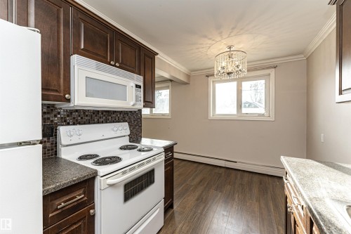 Kitchen featuring white appliances, a baseboard radiator, crown molding, dark brown cabinets, and dark wood-style floors - 102 10735 81 Avenue, Edmonton, AB - Indoor Photo Showing Kitchen