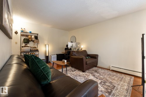 Living room featuring a baseboard radiator, wood finished floors, and a textured ceiling - 307 5730 Riverbend Road, Edmonton, AB - Indoor Photo Showing Living Room
