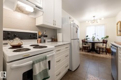 Kitchen with white appliances, white cabinetry, ventilation hood, light countertops, and dark tile patterned flooring - 