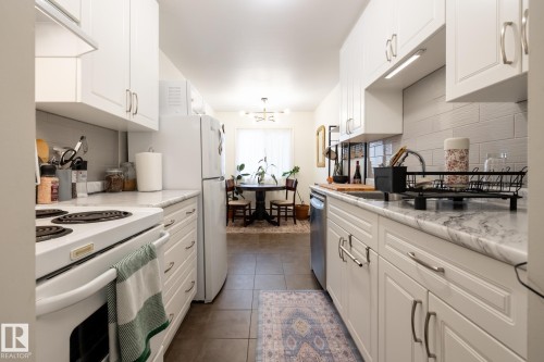 Kitchen featuring white appliances, white cabinets, dark tile patterned floors, and a chandelier - 307 5730 Riverbend Road, Edmonton, AB - Indoor Photo Showing Kitchen