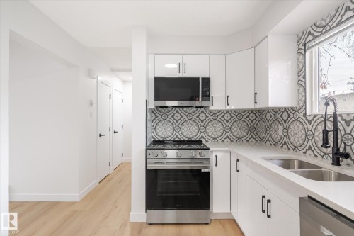Kitchen with stainless steel appliances, white cabinets, light stone counters, light wood-style floors, and tasteful backsplash - 5105 106A Street, Edmonton, AB - Indoor Photo Showing Kitchen With Double Sink