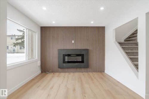 Unfurnished living room with an accent wall, a glass covered fireplace, wood finished floors, a textured ceiling, and stairs - 5105 106A Street, Edmonton, AB - Indoor Photo Showing Living Room With Fireplace