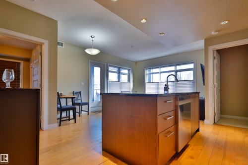 Kitchen featuring a kitchen island with sink, wood finish cabinetry, light wood-style floors, hanging light fixtures, and modern cabinets - 203 9908 84 Avenue, Edmonton, AB - Indoor