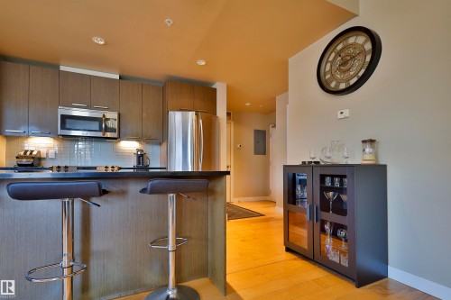 Kitchen featuring dark countertops, stainless steel appliances, a breakfast bar, light wood finished floors, and decorative backsplash - 203 9908 84 Avenue, Edmonton, AB - Indoor Photo Showing Kitchen With Stainless Steel Kitchen