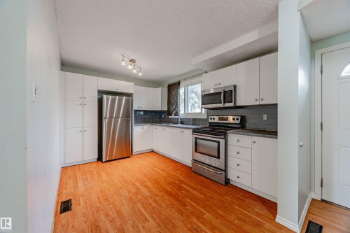Kitchen featuring stainless steel appliances, white cabinetry, laminate flooring, a textured ceiling, and designer tiled backsplash - 2551 135 Avenue, Edmonton, AB - Indoor Photo Showing Kitchen