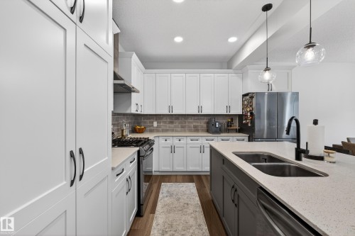 Kitchen featuring white cabinetry, stainless steel appliances, pendant lighting, dark wood-style floors, and a textured ceiling - 2098 Graydon Hill Crescent, Edmonton, AB - Indoor Photo Showing Kitchen With Double Sink With Upgraded Kitchen