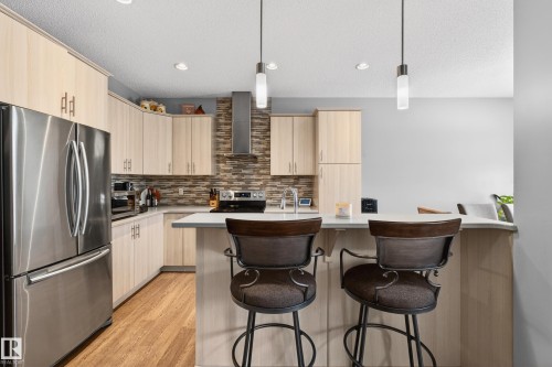 Kitchen with appliances with stainless steel finishes, a breakfast bar area, decorative light fixtures, light brown cabinetry, and a textured ceiling - 5910 Anthony Crescent, Edmonton, AB - Indoor Photo Showing Kitchen With Stainless Steel Kitchen