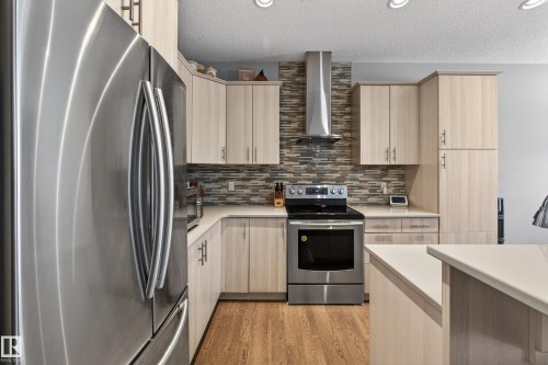 Kitchen featuring light brown cabinets, stainless steel appliances, wall chimney exhaust hood, tasteful backsplash, and light wood-type flooring - 5910 Anthony Crescent, Edmonton, AB - Indoor Photo Showing Kitchen With Stainless Steel Kitchen