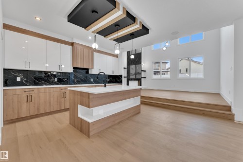 Dual tone kitchen with dual tone cabinetry, a kitchen island with sink, decorative light fixtures, light wood-type flooring, and light stone countertops - 733 Astoria Way, Devon, AB - Indoor Photo Showing Kitchen