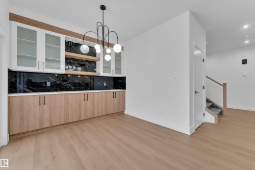 Bar featuring backsplash, glass fronted cabinets, light wood finished floors, light wood finish cabinets, and a chandelier - 733 Astoria Way, Devon, AB - Indoor Photo Showing Kitchen