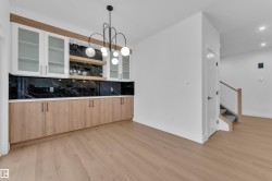 Bar featuring backsplash, glass fronted cabinets, light wood finished floors, light wood finish cabinets, and a chandelier - 
