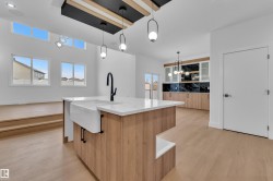 Kitchen featuring light wood finished floors, an island with sink, light stone counters, decorative backsplash, and two tone color scheme - 