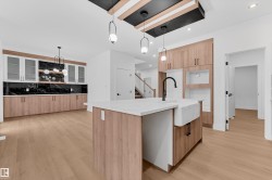Kitchen with light stone counters, light wood-type flooring, hanging light fixtures, and backsplash - 