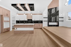 Two tone kitchen featuring decorative light fixtures, a center island with sink, light wood finished floors, decorative backsplash, and modern cabinets - 