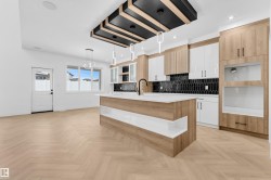 Two tone kitchen featuring two tone cabinets, hanging light fixtures, a center island with sink, open shelves, and decorative backsplash - 