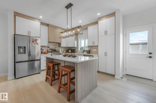 Dual tone kitchen featuring stainless steel appliances, a kitchen bar, light wood-style flooring, pendant lighting, and a center island - 21 Sienna Boulevard, Fort Saskatchewan, AB - Indoor Photo Showing Kitchen With Upgraded Kitchen