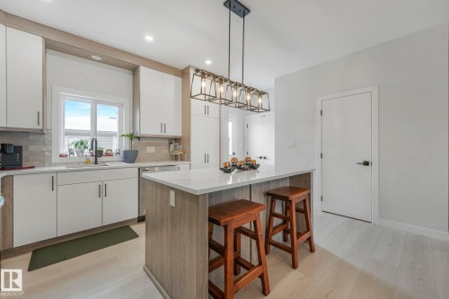 Dual tone kitchen with dual tone cabinetry, a kitchen bar, a center island, light wood-style floors, and hanging light fixtures - 21 Sienna Boulevard, Fort Saskatchewan, AB - Indoor Photo Showing Kitchen