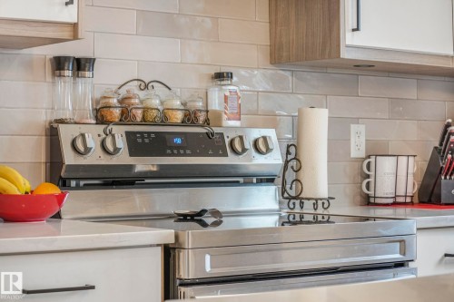 Kitchen view of stainless steel range with electric stovetop, tasteful backsplash, white cabinets, and light stone countertops - 21 Sienna Boulevard, Fort Saskatchewan, AB - Indoor Photo Showing Kitchen