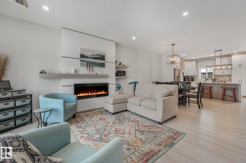 Living area featuring light wood-type flooring, a warm lit fireplace, and hanging lights - 21 Sienna Boulevard, Fort Saskatchewan, AB - Indoor Photo Showing Living Room With Fireplace