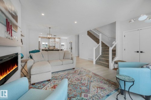 Living room featuring a lit fireplace, wood finished floors, and a chandelier - 21 Sienna Boulevard, Fort Saskatchewan, AB - Indoor Photo Showing Living Room With Fireplace