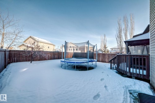 Yard covered in snow featuring a trampoline, a fenced backyard, a deck, and a residential view - 5814 165 Avenue, Edmonton, AB - Outdoor