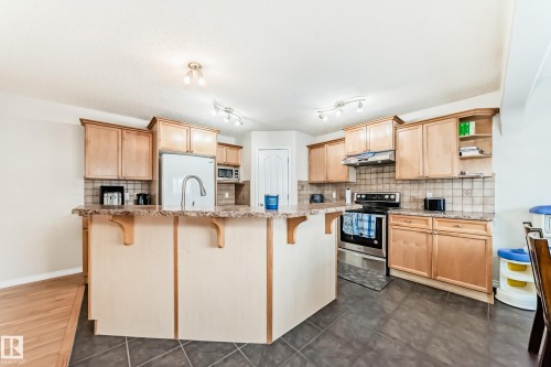 Kitchen featuring a breakfast bar area, light wood finish cabinetry, open shelves, and stainless steel appliances - 5814 165 Avenue, Edmonton, AB - Indoor Photo Showing Kitchen With Stainless Steel Kitchen