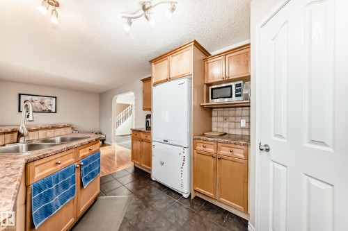 Kitchen with arched walkways, freestanding refrigerator, light countertops, light wood finish cabinetry, and a textured ceiling - 5814 165 Avenue, Edmonton, AB - Indoor Photo Showing Kitchen With Double Sink