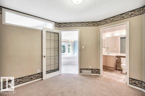 Unfurnished bedroom with light colored carpet, light tile patterned floors, a textured ceiling, a chandelier, and connected bathroom - 112 Haddow Close, Edmonton, AB - Indoor