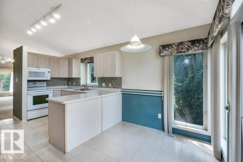 Kitchen with light countertops, white appliances, a peninsula, tasteful backsplash, and light wood finish cabinets - 112 Haddow Close, Edmonton, AB - Indoor Photo Showing Kitchen With Double Sink