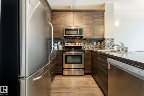 Kitchen featuring stainless steel appliances, light wood-type flooring, pendant lighting, a textured ceiling, and decorative backsplash - 407 2590 Anderson Way, Edmonton, AB - Indoor Photo Showing Kitchen With Double Sink