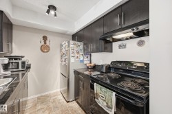 Kitchen featuring stainless steel appliances, under cabinet range hood, a textured ceiling, and dark cabinetry - 