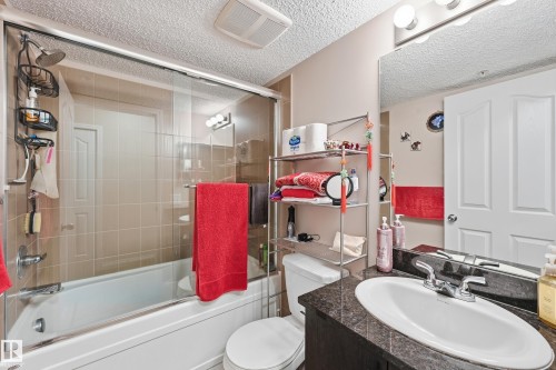 Bathroom featuring vanity, a textured ceiling, and shower / bath combination with glass door - 207 1080 Mcconachie Boulevard, Edmonton, AB - Indoor Photo Showing Bathroom