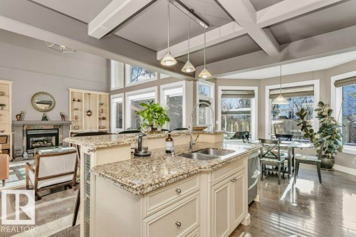Kitchen with light stone countertops, pendant lighting, light wood-type flooring, beam ceiling, and a kitchen island with sink - 1579 Hector Road, Edmonton, AB - Indoor Photo Showing Kitchen With Double Sink