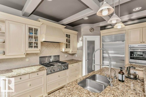 Kitchen with cream cabinetry, decorative light fixtures, light stone countertops, stainless steel appliances, and glass insert cabinets - 1579 Hector Road, Edmonton, AB - Indoor Photo Showing Kitchen With Double Sink With Upgraded Kitchen