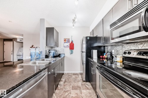 Kitchen with stainless steel appliances, decorative backsplash, a textured ceiling, gray cabinetry, and rail lighting - 302 530 Watt Boulevard Sw, Edmonton, AB - Indoor Photo Showing Kitchen With Stainless Steel Kitchen With Double Sink
