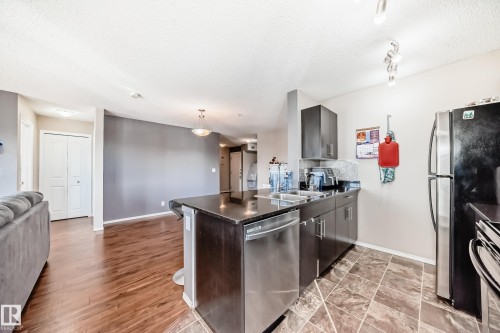 Kitchen with open floor plan, dishwasher, a peninsula, decorative light fixtures, and a textured ceiling - 302 530 Watt Boulevard Sw, Edmonton, AB - Indoor Photo Showing Kitchen With Stainless Steel Kitchen