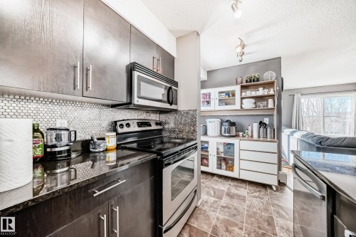 Kitchen featuring stainless steel appliances, track lighting, open shelves, tasteful backsplash, and a textured ceiling - 302 530 Watt Boulevard Sw, Edmonton, AB - Indoor Photo Showing Kitchen With Stainless Steel Kitchen With Upgraded Kitchen