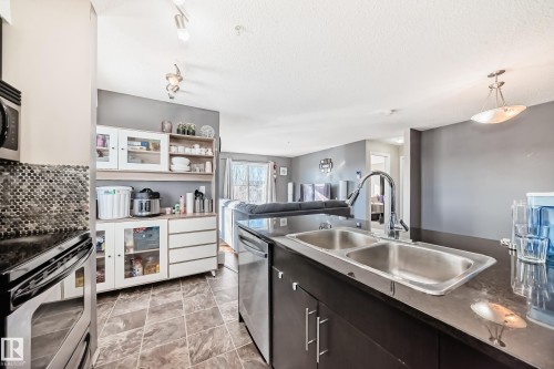 Kitchen featuring dark countertops, stainless steel appliances, open floor plan, a textured ceiling, and track lighting - 302 530 Watt Boulevard Sw, Edmonton, AB - Indoor Photo Showing Kitchen With Stainless Steel Kitchen With Double Sink