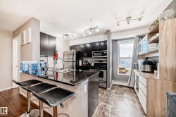 Kitchen featuring dark cabinets, stainless steel appliances, a breakfast bar area, dark stone counters, and a baseboard radiator - 