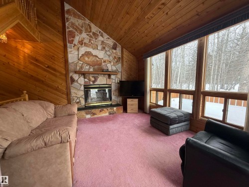 Carpeted living room featuring a fireplace, wood walls, and a vaulted wood ceiling - 34 Ella Mae Crescent, Rural Athabasca County, AB - Indoor Photo Showing Living Room With Fireplace