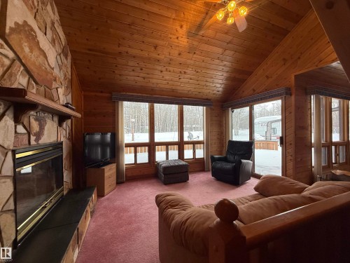 Living area with wood walls, carpet floors, a stone fireplace, a vaulted wooden ceiling, and plenty of natural light - 34 Ella Mae Crescent, Rural Athabasca County, AB - Indoor Photo Showing Living Room With Fireplace