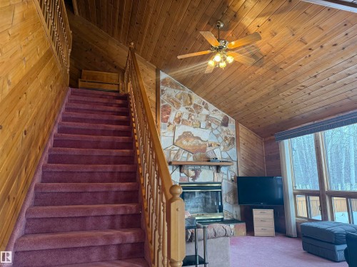 Stairway with a stone fireplace, wood walls, carpet floors, wood ceiling, and ceiling fan - 34 Ella Mae Crescent, Rural Athabasca County, AB - Indoor Photo Showing Other Room