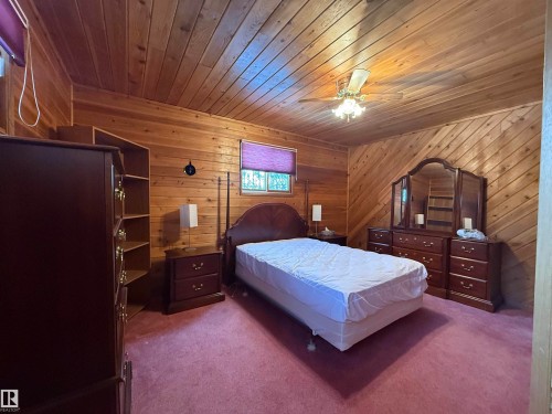 Carpeted bedroom featuring wooden walls, a ceiling fan, and wood ceiling - 34 Ella Mae Crescent, Rural Athabasca County, AB - Indoor Photo Showing Bedroom