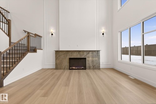Unfurnished living room featuring a high ceiling, plenty of natural light, light wood finished floors, and a fireplace - 9 Elwyck Gate, Spruce Grove, AB - Indoor With Fireplace