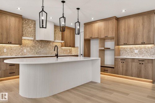 Kitchen featuring wood finish cabinetry, light stone counters, light wood-type flooring, hanging light fixtures, and modern cabinets - 9 Elwyck Gate, Spruce Grove, AB - Indoor Photo Showing Kitchen With Upgraded Kitchen