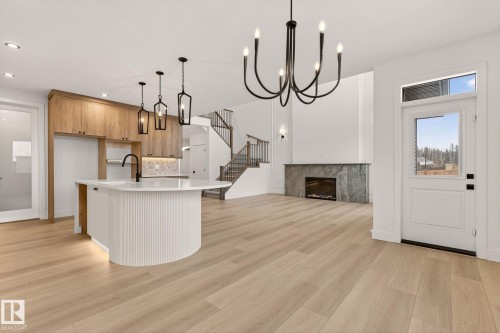Kitchen with a kitchen island with sink, open floor plan, a fireplace, a chandelier, and light wood finished floors - 9 Elwyck Gate, Spruce Grove, AB - Indoor Photo Showing Kitchen